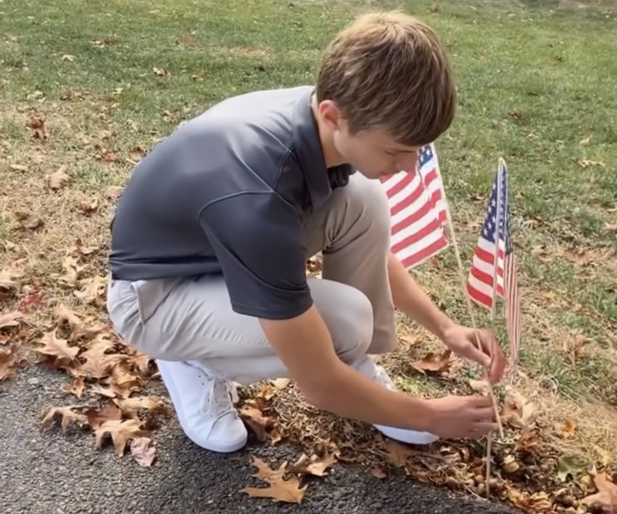 student planting American flags near a sidewalk