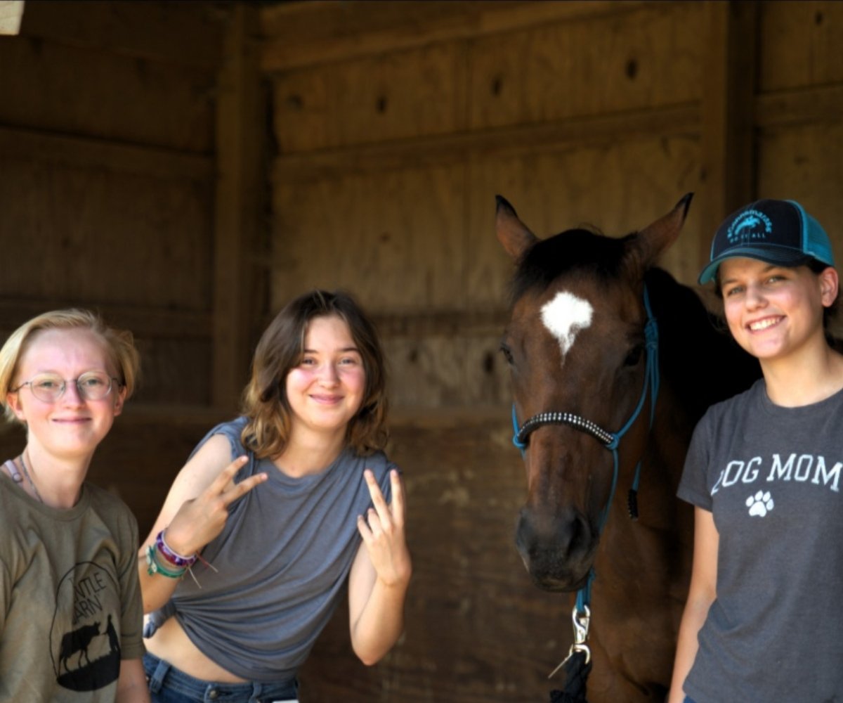 three students with a horse in a stable