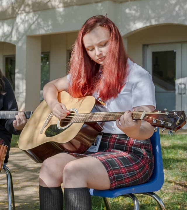 student playing acoustic guitar outside
